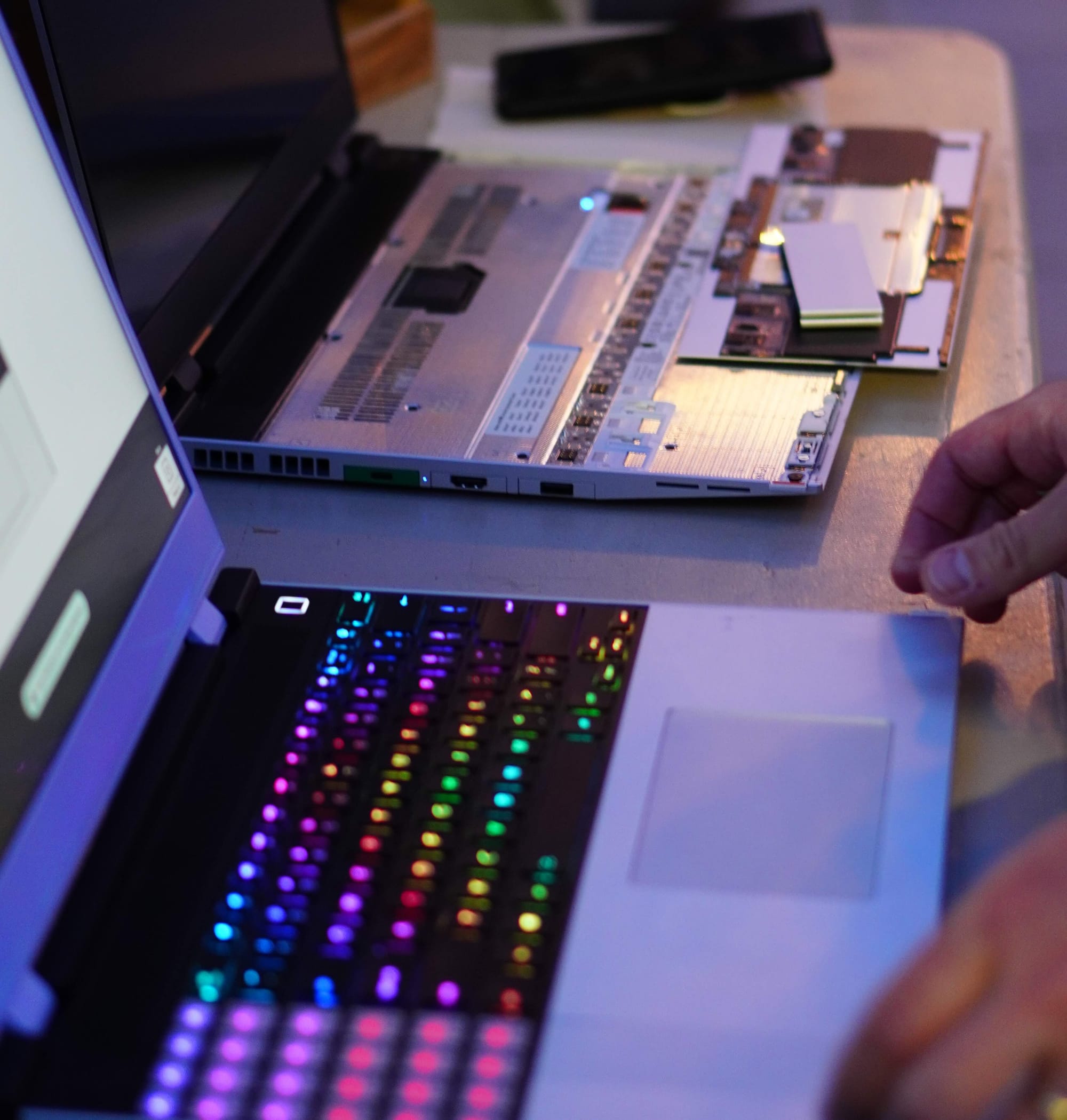 A picture of two framework laptops side by side. On the left framework is a rainbow keyboard. The right framework is missing it's keyboard and trackpad. It has a pile of parts from the first on top as they were testing hot-swapping parts.